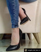 Load image into Gallery viewer, Black high-heeled shoes worn with blue jeans on a light-colored chair.