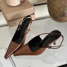Load image into Gallery viewer, Brown high-heeled shoes on a glass surface with a box and decorative item in the background.