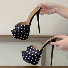 Load image into Gallery viewer, Black high-heeled shoes with white polka dots held by a hand against a neutral background