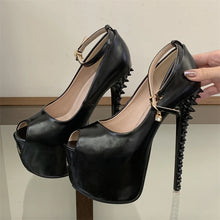 Load image into Gallery viewer, A pair of black peep-toe high heels with spiked stiletto heels and ankle straps, shown with a hand holding one shoe against an indoor neutral background.