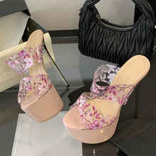 Load image into Gallery viewer, Floral high-heeled shoes on a reflective surface with a black handbag in the background.