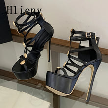 Load image into Gallery viewer, A pair of black strappy high-heeled sandals with platform soles, ankle straps, and gold-tone hardware, displayed on a glass shelf against a neutral indoor background.