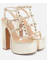 Load image into Gallery viewer, A pair of metallic champagne gold platform high-heel sandals with multiple strappy details and pyramid stud embellishments, shown against a plain light gray background.