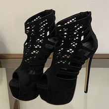 Load image into Gallery viewer, Black high-heeled shoes with cut-out design on a reflective surface.