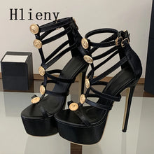 Load image into Gallery viewer, A pair of black strappy high-heeled sandals with platform soles and large gold-tone decorative buttons, displayed on a reflective surface with a black box in the background. The brand name 'HlienY' is visible in the top left corner.