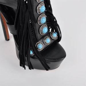 Black high-heeled shoe with turquoise embellishments and fringes on a light gray background