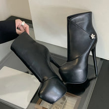 Load image into Gallery viewer, Black high-heeled boots with a decorative flower on a reflective surface.