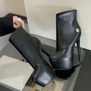 Black high-heeled boots with a decorative flower on a reflective surface.