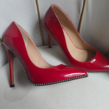 Load image into Gallery viewer, Red high-heeled shoes with studded details on a light gray background
