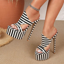 Load image into Gallery viewer, A pair of women's platform high-heel sandals with bold black and white horizontal stripes, shown on a model's feet. The shoes feature wraparound straps, a chunky platform sole, and slim stiletto heels.