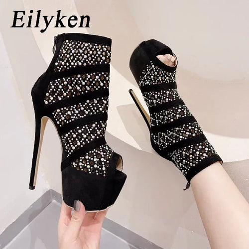 Black high-heeled open-toe shoes with rhinestone detailing, held by a hand.