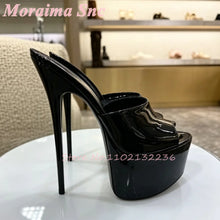 Load image into Gallery viewer, A pair of black patent leather high-heeled platform sandals with slingback straps, displayed on a white round table in a store setting. The brand name 'Moraima Snc' is written in pink text at the top left, and a store number watermark is present near the bottom.