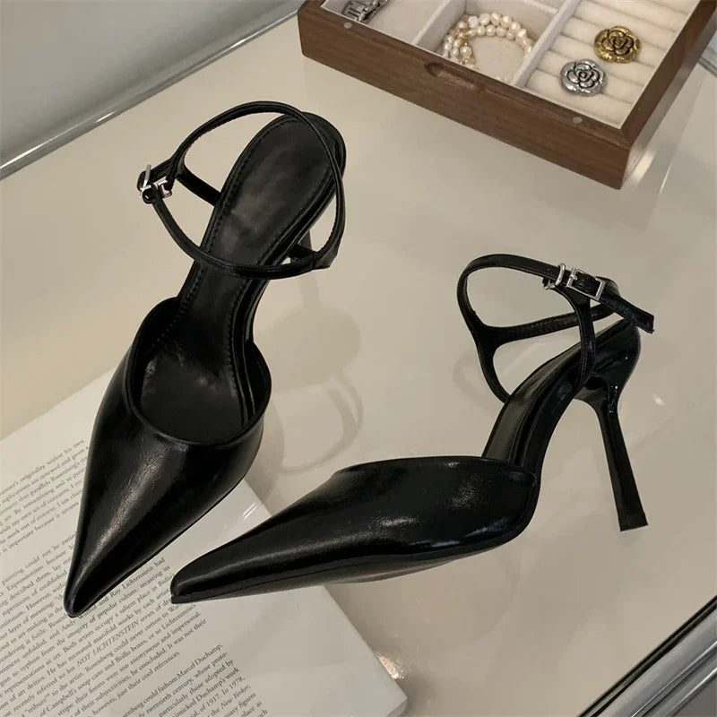 Black high-heeled shoes on a light surface with jewelry in the background
