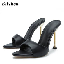 Load image into Gallery viewer, A pair of black leather slide high heels with a double strap design and slim gold stiletto heels, shown on a white background with the brand name Eilyken in the top left corner.