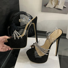 Load image into Gallery viewer, Black high-heeled shoes with clear straps on a white surface, with a hand holding one shoe.