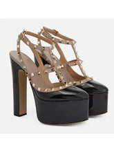 Load image into Gallery viewer, A pair of black patent leather high-heeled platform sandals with beige leather straps and gold-tone pyramid studs, shown against a plain light gray background.