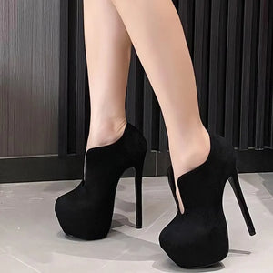 Black high-heeled platform shoes worn by a person on a neutral background