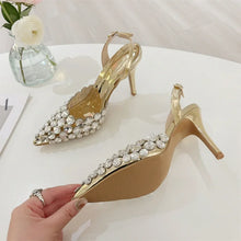Load image into Gallery viewer, Gold high-heeled shoes with crystal embellishments on a white surface, held by a hand.