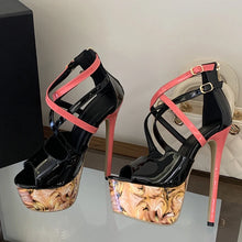 Load image into Gallery viewer, A pair of high-heeled platform sandals with glossy black patent leather uppers, bright pink straps, and a marbled beige and gold floral print on the platform soles, displayed on a reflective surface.