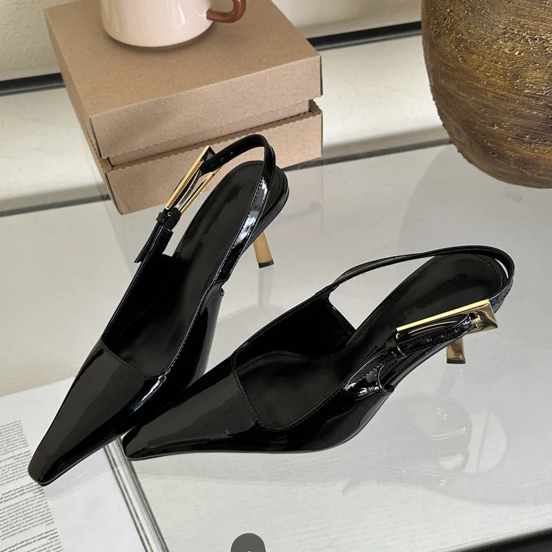 Black high-heeled shoes with gold accents on a reflective surface.