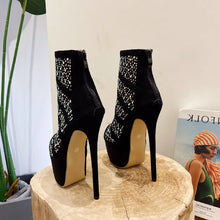 Load image into Gallery viewer, Black high-heeled boots with rhinestone details on a wooden block, with a magazine in the background.