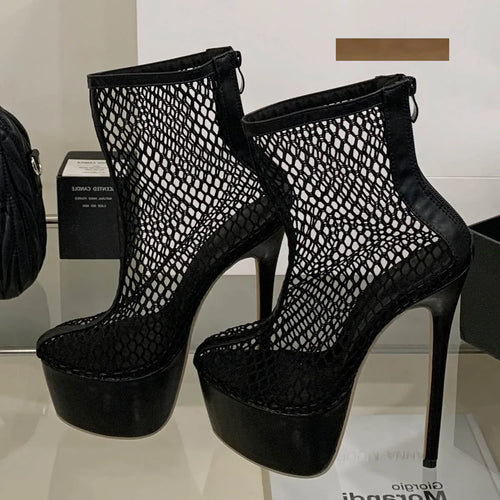 Black mesh platform high-heeled shoes on a reflective surface with a blurred background.