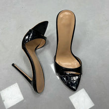 Load image into Gallery viewer, A pair of black patent leather high-heeled mule sandals with a crocodile-embossed pattern on the toe strap, displayed on a gray concrete floor.