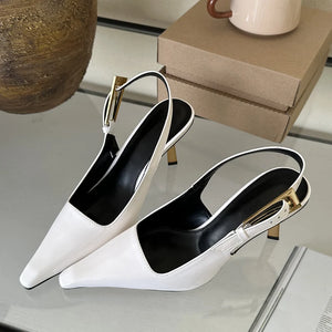 White and black pointed-toe slingback heels with gold accents on a reflective surface.