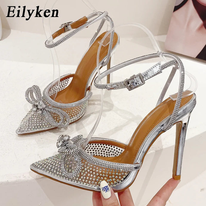 Silver high-heeled shoes with rhinestone details on a white background, featuring the brand 'Eilyken'.