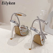 Load image into Gallery viewer, High-heeled shoes with clear straps and beige soles on a white background, branded &#39;Eilyken&#39;.