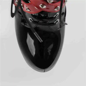 Black high-heeled shoe with red studded detail on a light gray background