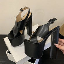 Load image into Gallery viewer, Black high-heeled sandals on a white platform with a hand pointing to the heel.
