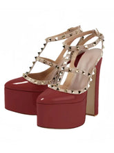 Load image into Gallery viewer, A pair of high-heeled platform sandals with glossy red patent leather toe caps and stacked platform heels, decorated with beige faux-leather straps and gold-tone pyramid studs, shown against a plain white background.