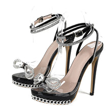 Load image into Gallery viewer, Black high-heeled sandals with clear platform and decorative straps on a white background