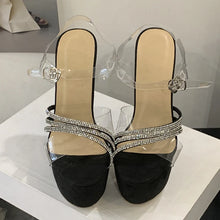 Load image into Gallery viewer, Black high-heeled shoes with clear straps and rhinestone embellishments on a white surface.
